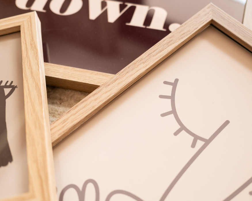3 posters, waarvan 1 beige poster met line art erop. 1 poster met een lichtbruine kleur en 1 poster in bordeaux kleur. De eikenhouten lijsten eromheen geven een rustige uitstraling.