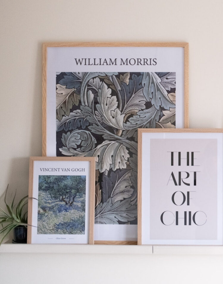 Recht vooraanzicht van een compositie met drie ingelijste posters op een schilderijplank: een grote William Morris poster, Vincent van Gogh's Olive Grove en een 'The Art of Chic' typografie poster in houten fotolijsten.