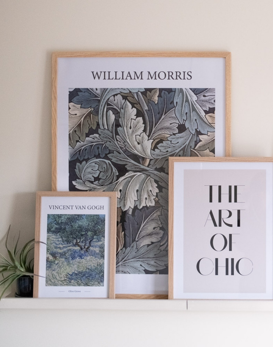 Recht vooraanzicht van een compositie met drie ingelijste posters op een schilderijplank: een grote William Morris poster, Vincent van Gogh's Olive Grove en een 'The Art of Chic' typografie poster in houten fotolijsten.