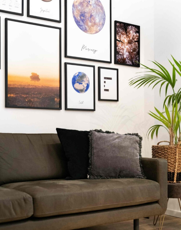 Sfeervolle fotowand boven een donkergrijze bank met diverse zwarte fotolijsten, waaronder planetenposters, natuurfoto's en een quote poster, gestyled naast een grote kamerplant.