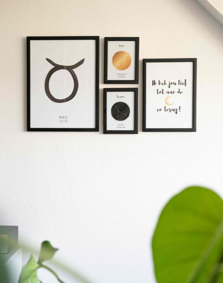 Fotowand aan een witte muur met vier zwarte fotolijsten, bestaand uit gepersonaliseerde sterrenbeeldposters voor Maartje (Stier), Fien (Schorpioen) en Bram (Kreeft), gecombineerd met een quote poster 'Ik heb jou lief tot aan de maan en terug!'.