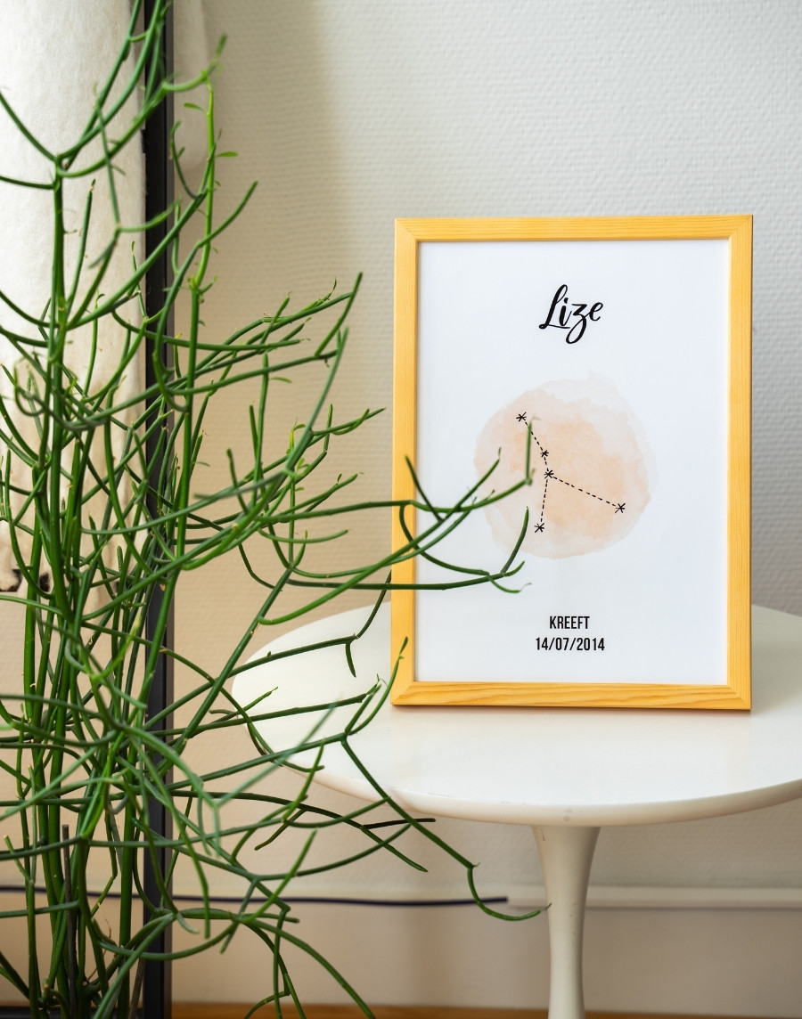 Ingelijste poster van het sterrenbeeld Kreeft gepersonaliseerd met de naam Lize en datum, in een houten lijst op een wit ronde bijzettafel naast een groene potplant.
