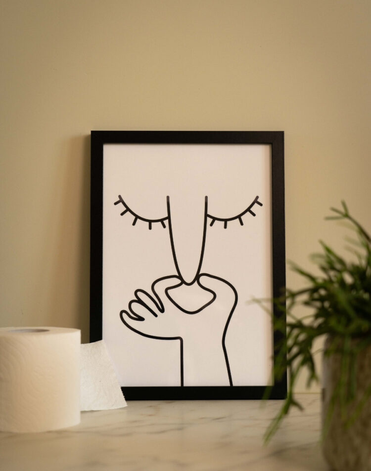 Ingelijste toiletposter met een minimalistische line art illustratie van een gezicht dat de neus dichtknijpt in een schwarze fotolijst, gestyled naast een rol toiletpapier.