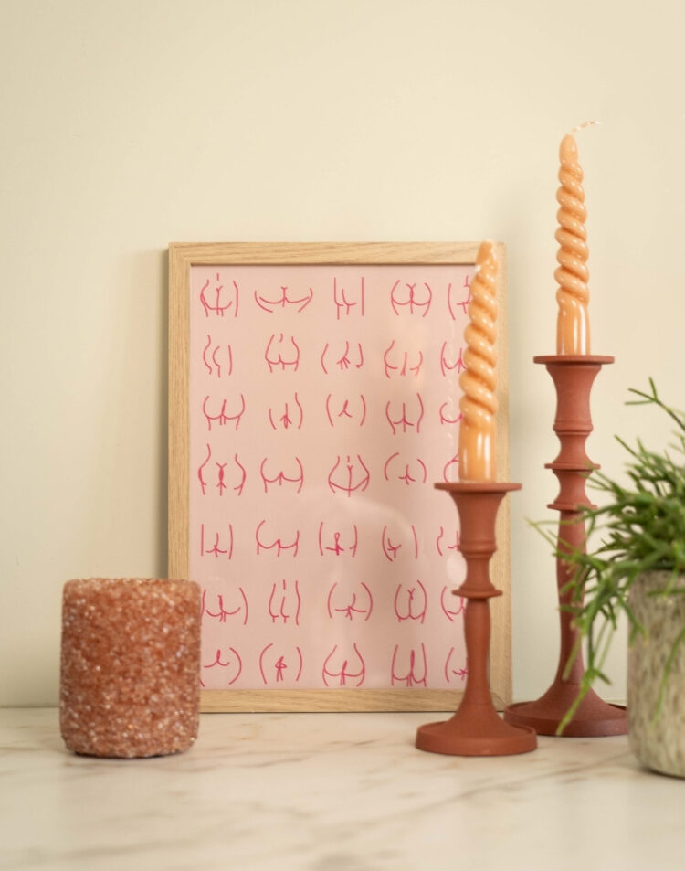 Ingelijste roze poster met een minimalistische line art illustratie van verschillende billen in een houten lijst, gestyled met terra kandelaars en kaarsen op een marmeren ondergrond.
