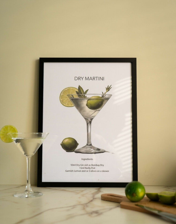 Ingelijste poster met een illustratie en recept van een Dry Martini cocktail in een zwarte lijst, staand op een marmeren aanrecht naast een Martini glas en limoenen.