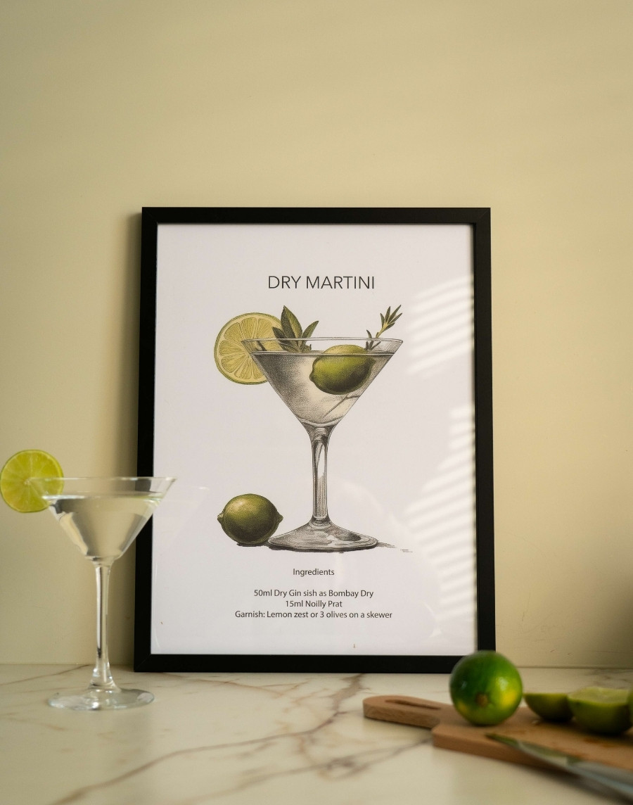 Ingelijste poster met een illustratie en recept van een Dry Martini cocktail in een zwarte lijst, staand op een marmeren aanrecht naast een Martini glas en limoenen.