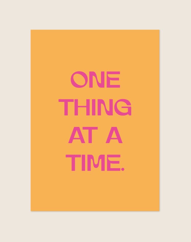 Retro oranje Poster One thing met felle roze letters en de tekst One thing at a time, sfeervol opgehangen in een werkkamer.