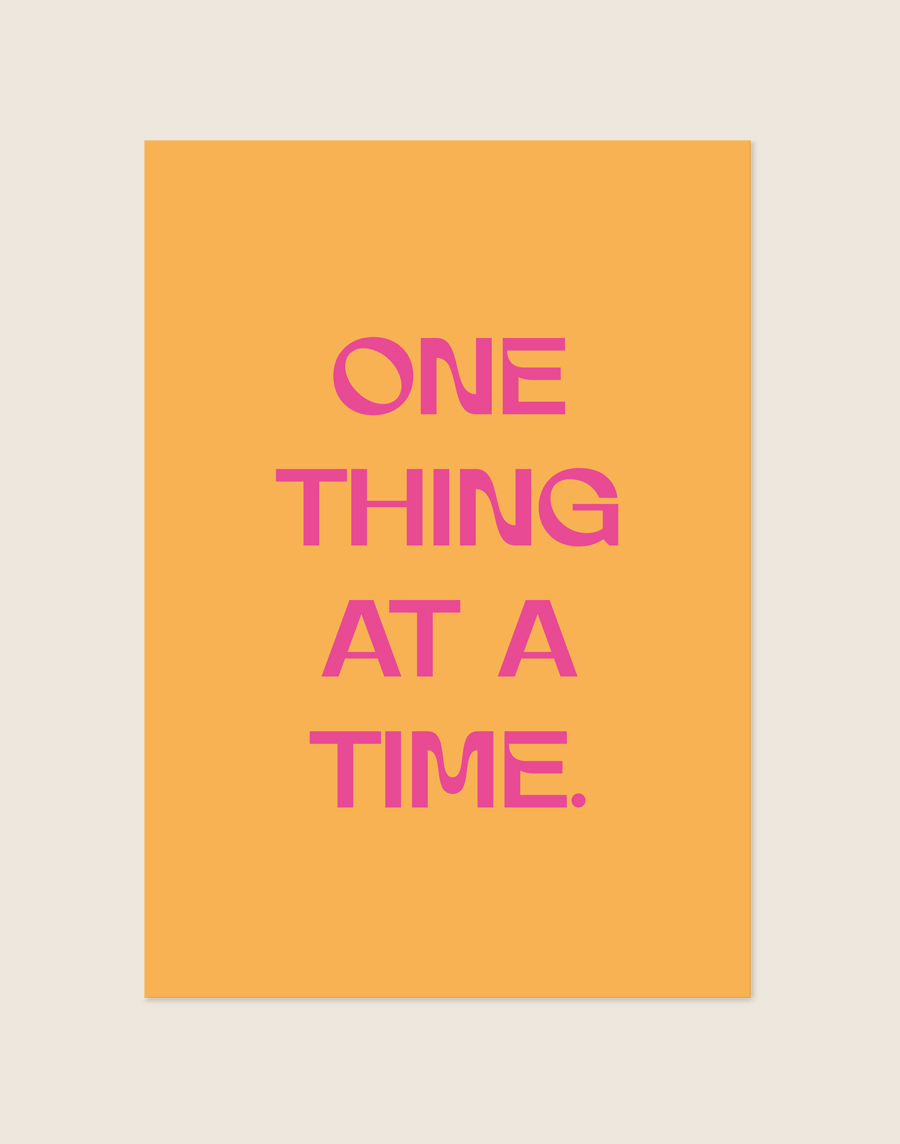 Retro oranje Poster One thing met felle roze letters en de tekst One thing at a time, sfeervol opgehangen in een werkkamer.