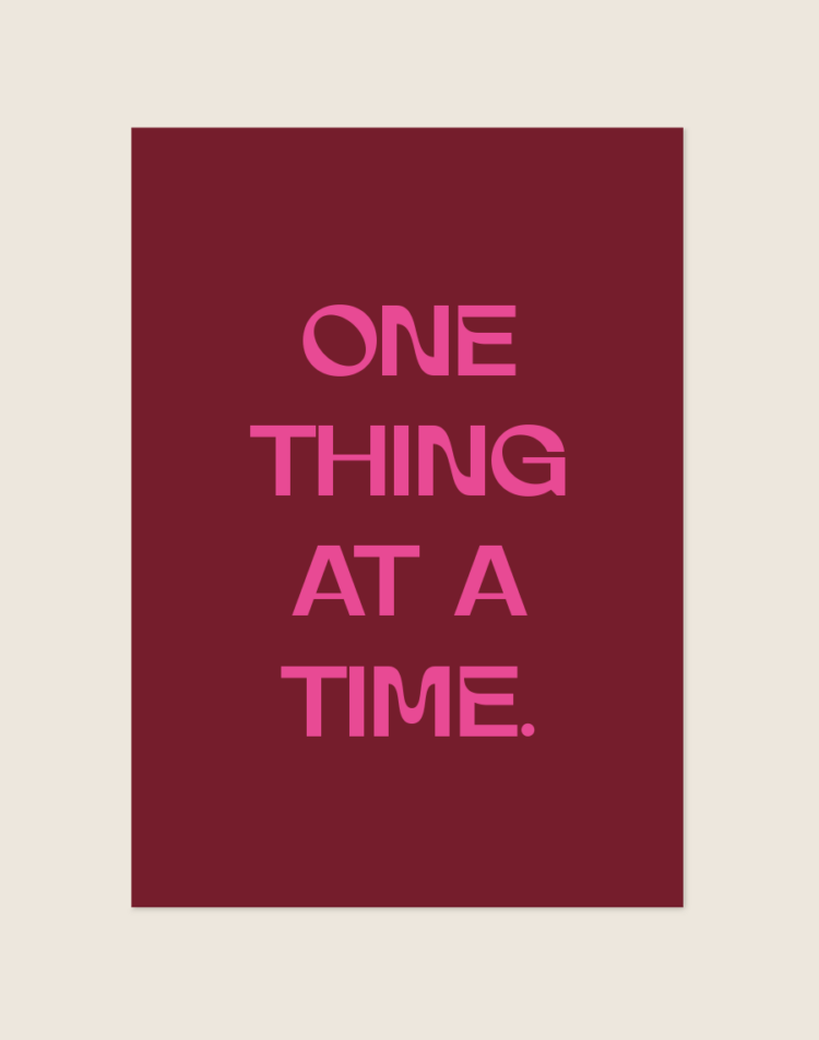 Een rechthoekige poster, gecentreerd tegen een effen, lichtbeige achtergrond. De poster zelf heeft een warme, dieprode (bordeauxrode) achtergrondkleur. In het midden staat de motiverende quote 'ONE THING AT A TIME.' geschreven in opvallende, felroze letters. De tekst is gecentreerd en verdeeld over vier regels. Het lettertype is dik en heeft speelse, licht golvende lijnen, wat het ontwerp een subtiele, moderne retro uitstraling geeft.