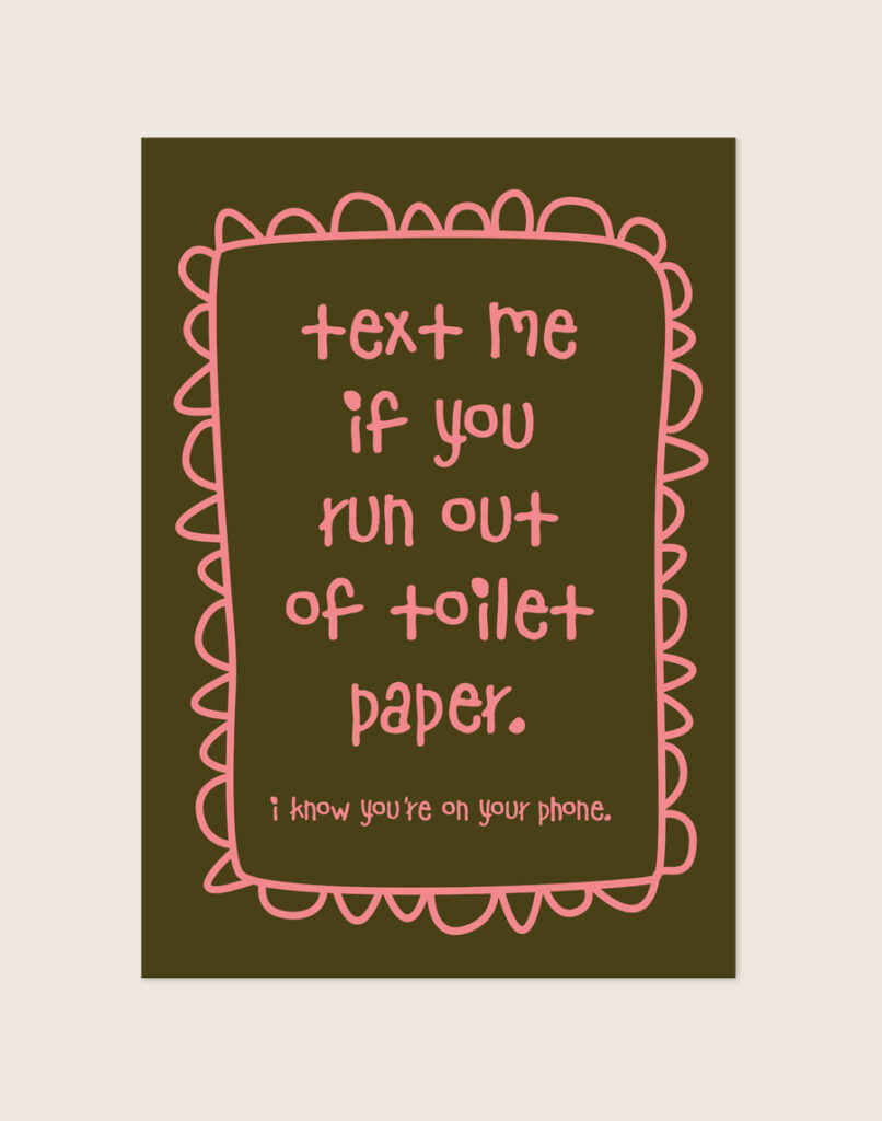 Warme diepbruine poster met roze handgeschreven tekst text me if you run out of toilet paper i know you're on your phone en een gegolfde rand, sfeervol opgehangen aan een neutrale muur in een moderne toiletruimte.
