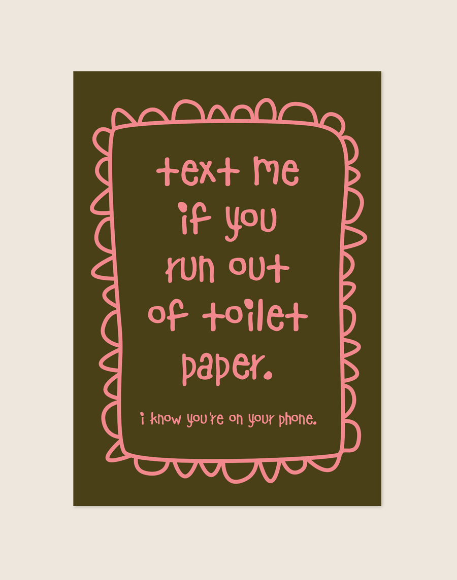 Warme diepbruine poster met roze handgeschreven tekst text me if you run out of toilet paper i know you're on your phone en een gegolfde rand, sfeervol opgehangen aan een neutrale muur in een moderne toiletruimte.