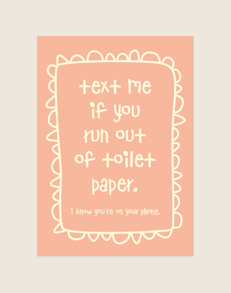 Zacht perzikroze poster met crèmekleurige handgeschreven tekst text me if you run out of toilet paper en een gegolfde rand, sfeervol opgehangen aan een neutrale muur in een moderne toiletruimte.