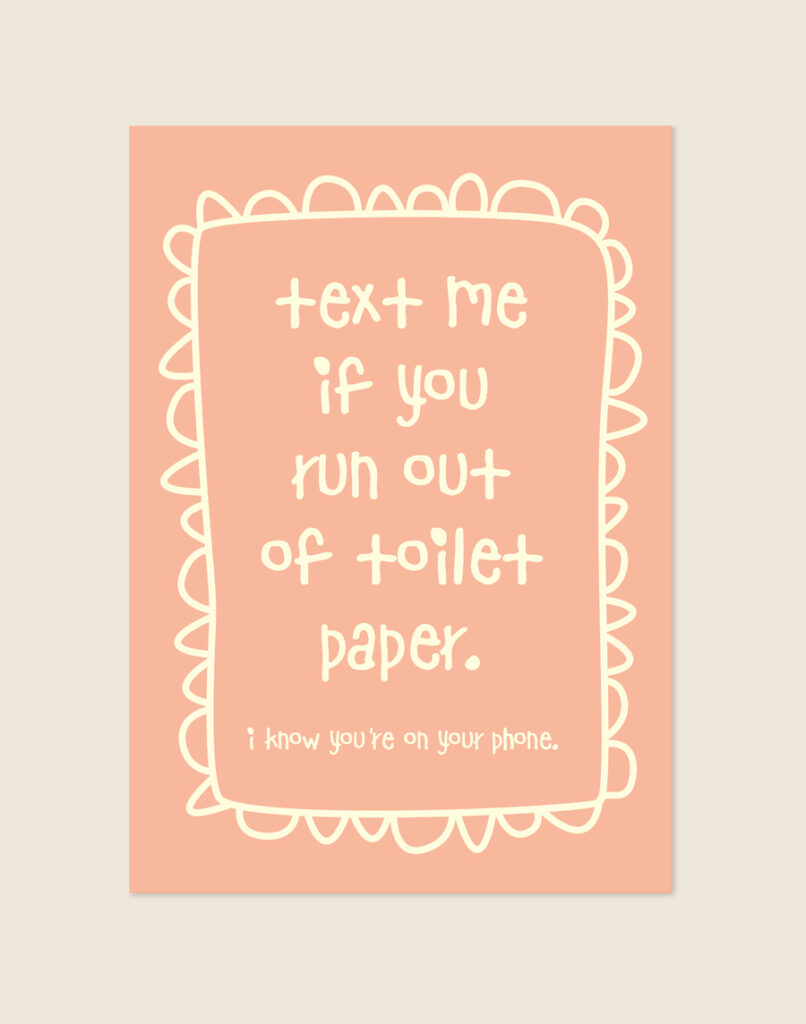Zacht perzikroze poster met crèmekleurige handgeschreven tekst text me if you run out of toilet paper en een gegolfde rand, sfeervol opgehangen aan een neutrale muur in een moderne toiletruimte.