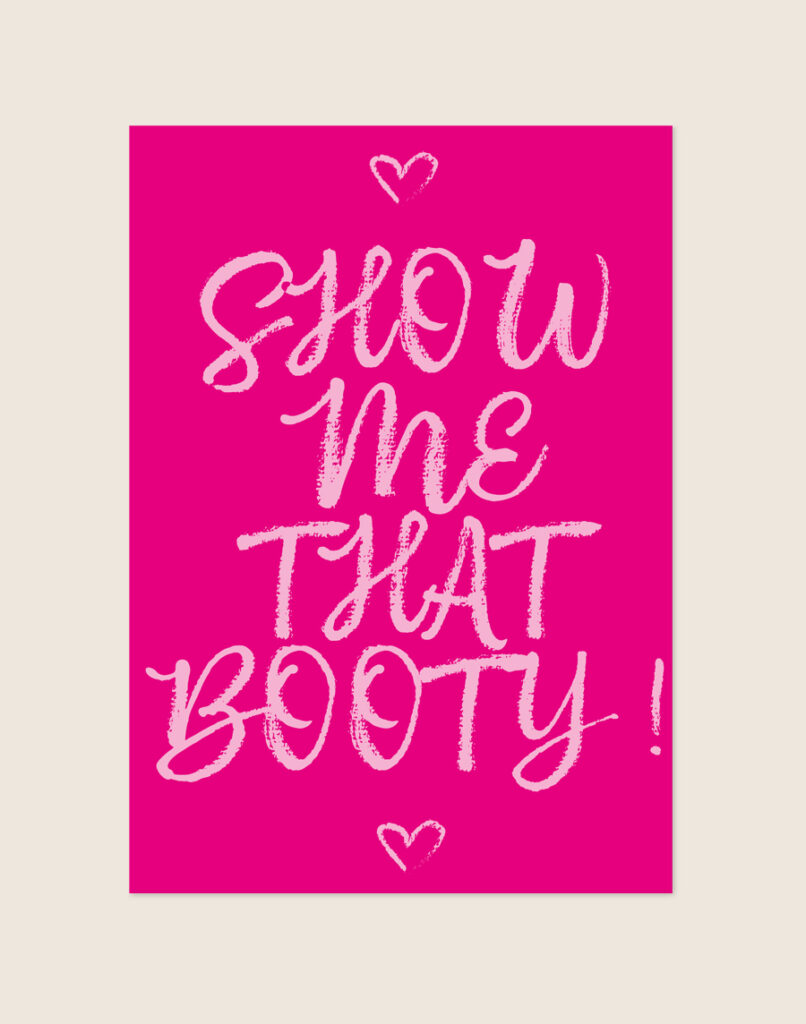 Felle magentaroze poster met lichtroze handgeschreven letters met de tekst SHOW me THAT BOOTY! en twee hartjes, sfeervol opgehangen aan een neutrale muur in een moderne toiletruimte.