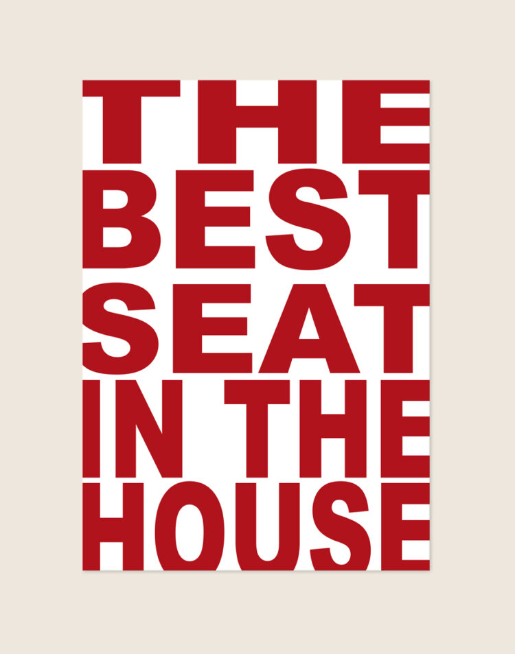 Opvallende witte poster met grote rode blokletters en de tekst The Best Seat In The House, sfeervol opgehangen aan een neutrale muur in een moderne toiletruimte.