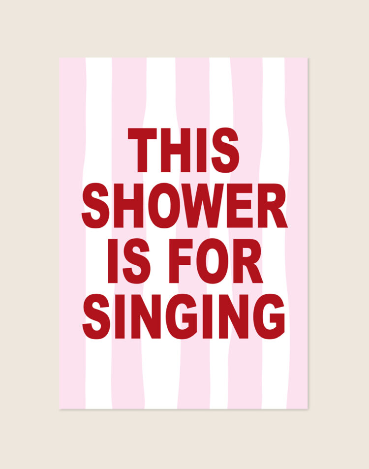 Trendy typografische poster met roze-witte strepen en rode tekst This shower is for singing, sfeervol opgehangen aan een neutrale muur in een moderne badkamer.