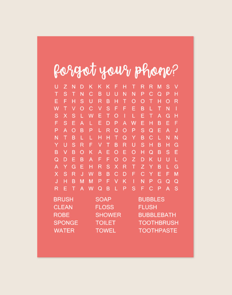 Vrolijke koraalrode poster met een witte woordzoeker en de tekst forgot your phone?, sfeervol opgehangen aan een neutrale muur in een moderne toiletruimte.