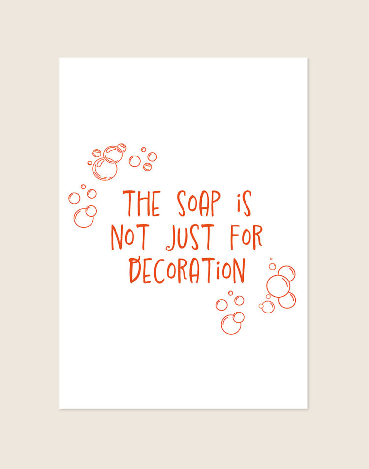 Humoristische badkamer Poster Decoration met de oranje tekst "The soap is not just for decoration" en speelse zeepbellen op een helderwitte achtergrond, sfeervol opgehangen in een ruimte.