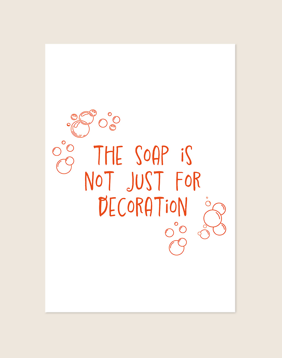 Humoristische badkamer Poster Decoration met de oranje tekst "The soap is not just for decoration" en speelse zeepbellen op een helderwitte achtergrond, sfeervol opgehangen in een ruimte.