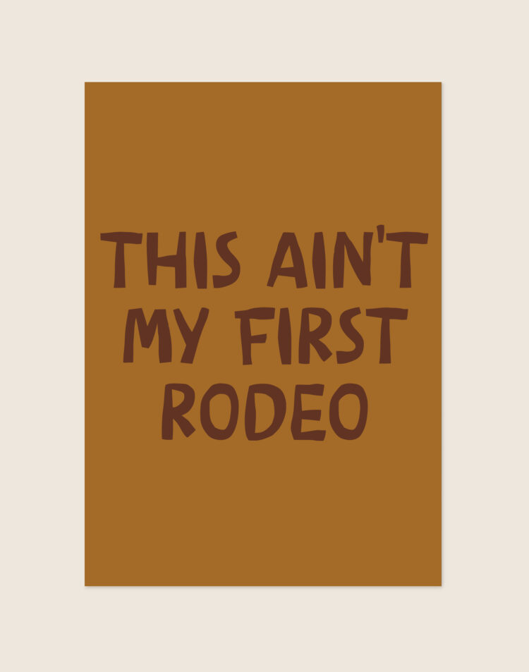 Een rechthoekige typografische poster met een warme, okerbruine achtergrond. In het midden staat de grappige quote 'THIS AIN'T MY FIRST RODEO' gecentreerd verdeeld over vier regels. De tekst is geschreven in dikke, donkerbruine blokletters met een speelse, onregelmatige vorm die lijkt op uitgeknipt papier.