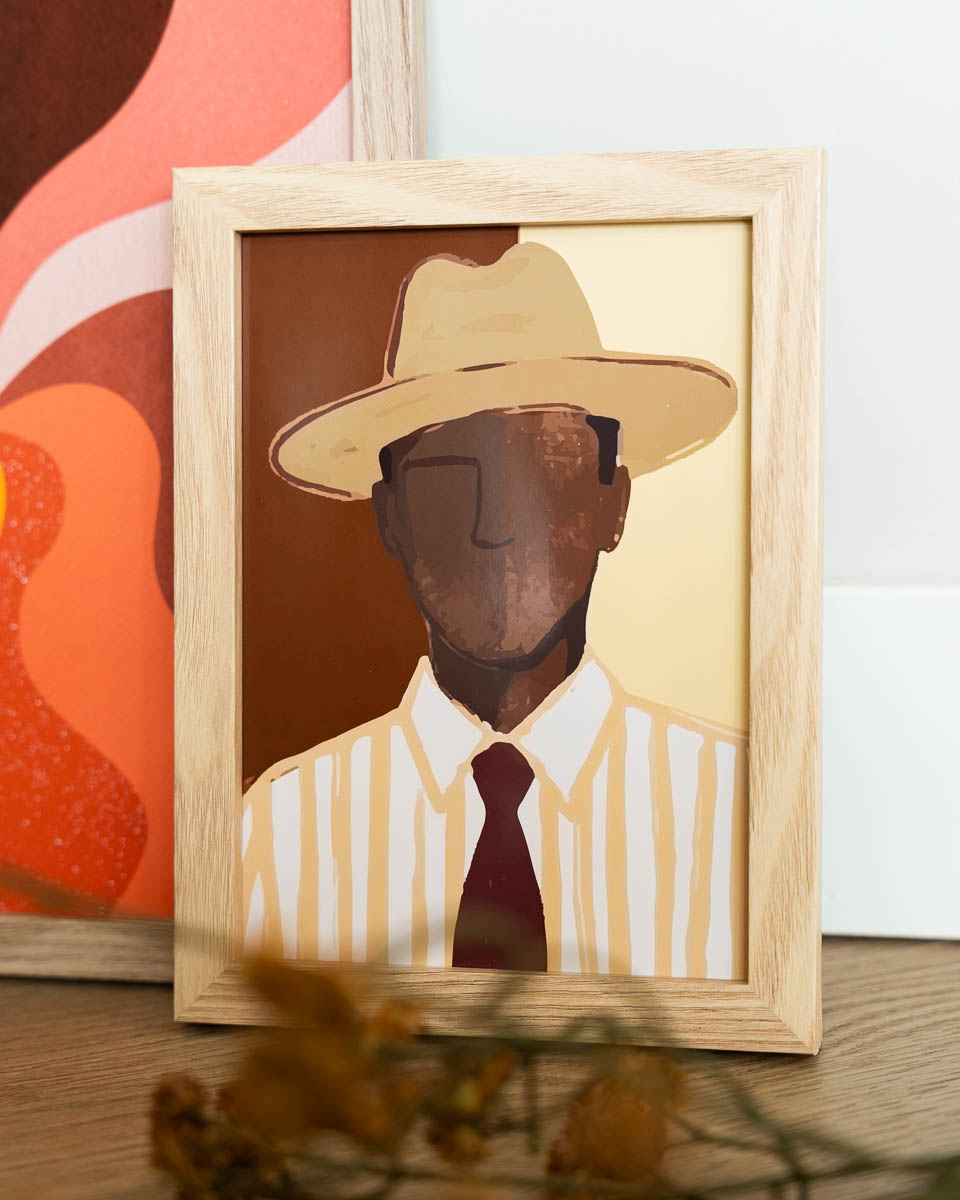 Een houten schilderijlijst met een artistieke illustratie van een man met een hoed, gestreept overhemd en een donkere stropdas. Het portret is opgebouwd uit aardetinten zoals bruin, beige en geel. Op de achtergrond is een gedeelte van een andere kleurrijke poster te zien.